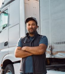 Confident truck driver standing outdoors with arms crossed and looking at camera. Copy space.
